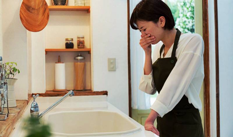 Woman in black white dress closing her noise with her hand inside a kitchen