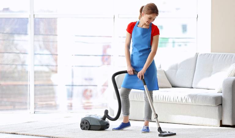 Woman in red blue dress vacuuming inside a bedroom