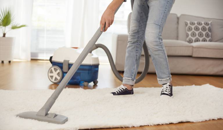 Woman cleaning carpet with a vacuum cleaner in room