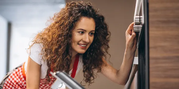Woman with curly hair holding a brush in her hand and looking at her oven