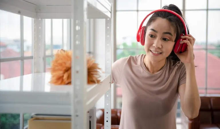 Smiling woman holding her headphone and cleaning with a duster.