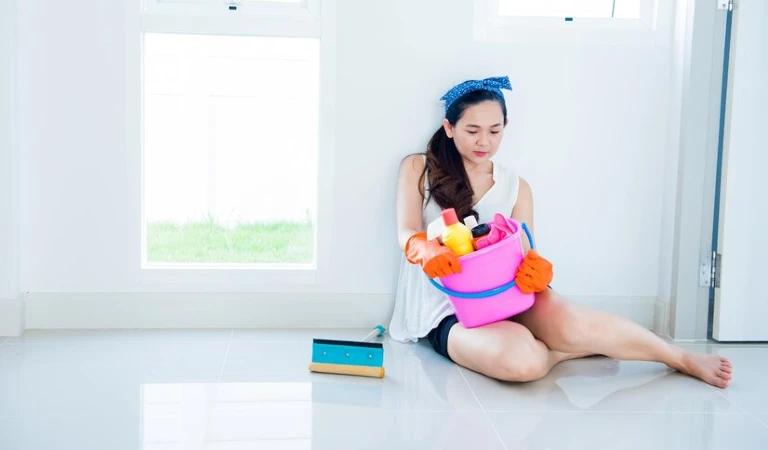 Woman in floor with a cleaning basket filled with cleaning products and tools.