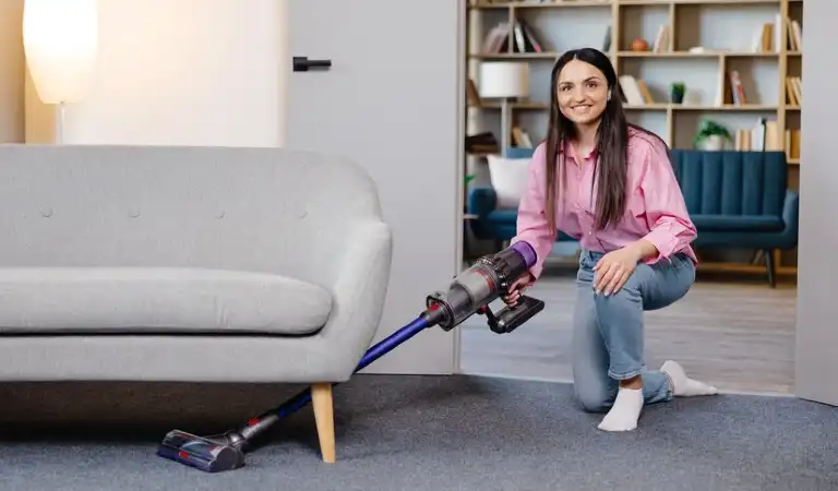 A lady in pink dress cleaning floor using cordless vacuum cleaner.