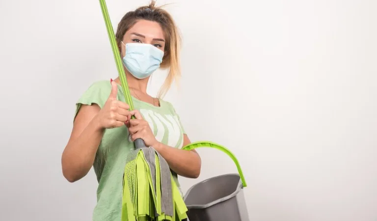 A lady in green top holding a basket and a stick in her hand showing her thumps up.