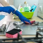 Woman cleaning stainless steel gas surface in the kitchen with rubber gloves