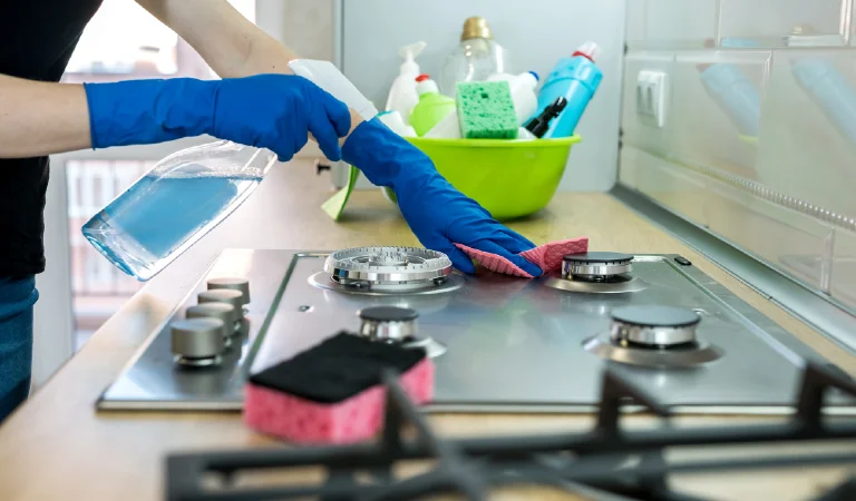 Woman cleaning stainless steel gas surface in the kitchen with rubber gloves