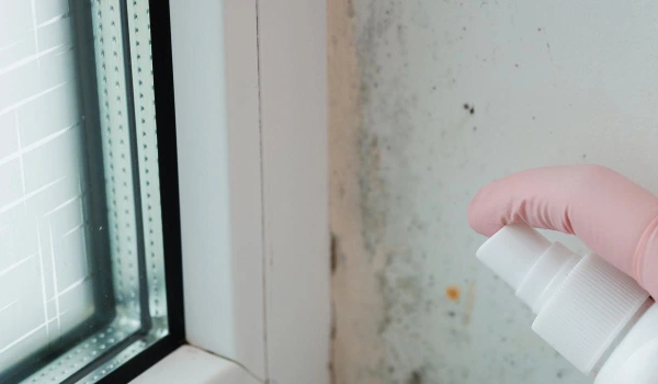 Molded bathroom and person in professional protection suit spraying chemicals to kill the mold