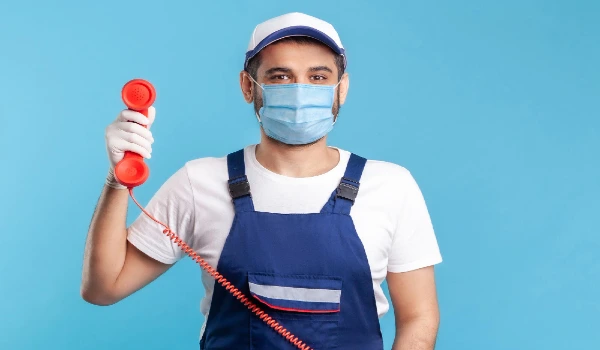 Housing maintenance call centre. Friendly handyman in overalls, mask, safety gloves, answering customer call