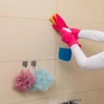 A woman engaged in the task of thoroughly cleaning bathroom tiles using sponges and gloves