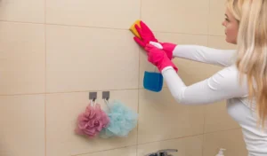 A woman engaged in the task of thoroughly cleaning bathroom tiles using sponges and gloves