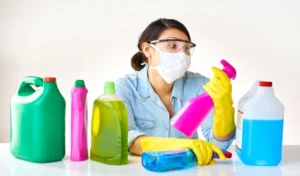 Detergent bottles gloves and woman with mask or glasses for protection safety and cleaning at home housekeeping cleaner