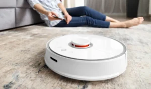 A girl sits on the floor in the living room and controls a robotic vacuum cleaner using a smartphone