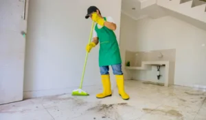 Male janitor clean floor with broom in dirty house