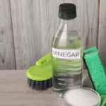 Natural cleaning products vinegar in bottle baking soda glove sponge and brush on light wooden table