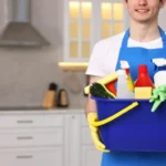 Cleaning service worker holding bucket with supplies in kitchen closeup