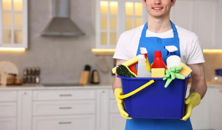Cleaning service worker holding bucket with supplies in kitchen closeup